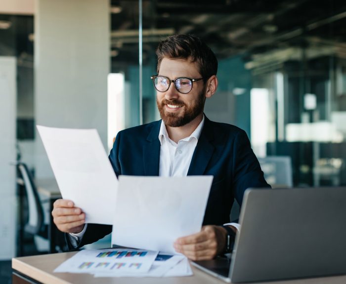 feliz-hombre-negocios-leyendo-documentos-e-informes-comerciales-regocijandose-asuntos-empresa-sentados-oficina-moderna